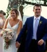 Bride and groom smiling while walking hand-in-hand at their wedding, with the bride holding a bouquet.