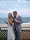 Bride and groom laughing while holding drinks on a beachside deck during their wedding.